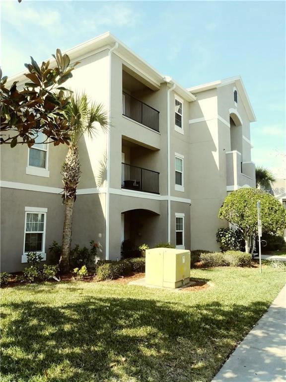 A three-story apartment building exterior features beige stucco walls, balconies, and a yellow utility box — 6512 SWISSCO DRIVE UNIT 1423, ORLANDO, FL