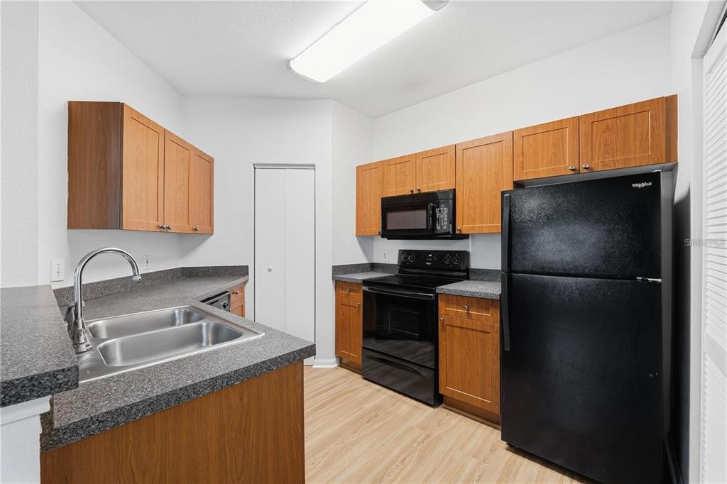 A kitchen features wood cabinets, black appliances, gray countertops, and light-colored wood-look flooring — 2249 PORTOFINO PLACE UNIT 22-2217, PALM HARBOR, FL