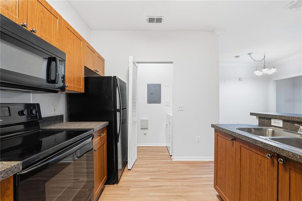 A kitchen with wood cabinets, black appliances, and a doorway leading to a laundry area — 2249 PORTOFINO PLACE UNIT 22-2217, PALM HARBOR, FL
