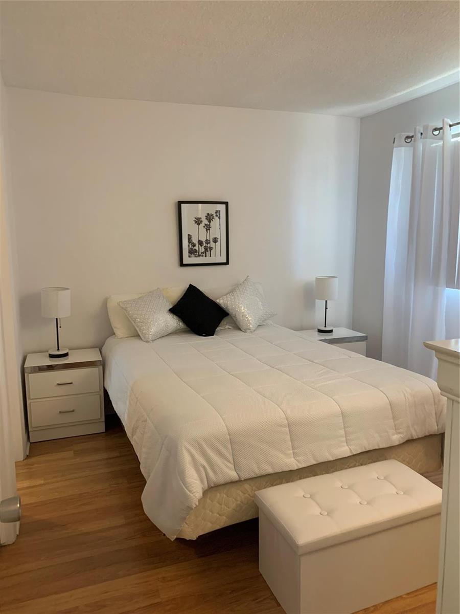 A bedroom features a white bed, two nightstands with lamps, and a white storage bench — 2751 Golf Boulevard # 2028, Pompano Beach FL 33064, POMPANO BEACH, FL