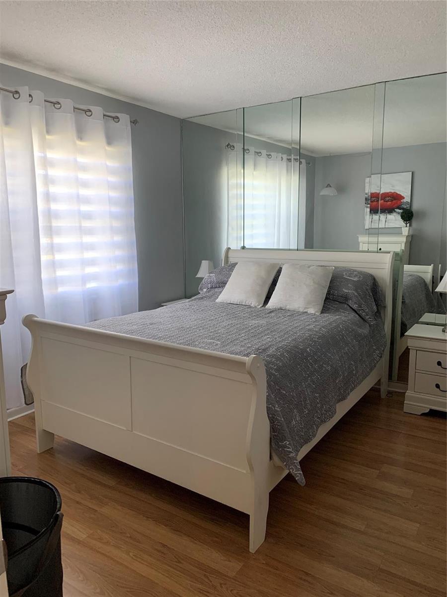 A bedroom features a white sleigh bed, wood-look flooring, and a mirrored wall behind it — 2751 Golf Boulevard # 2028, Pompano Beach FL 33064, POMPANO BEACH, FL