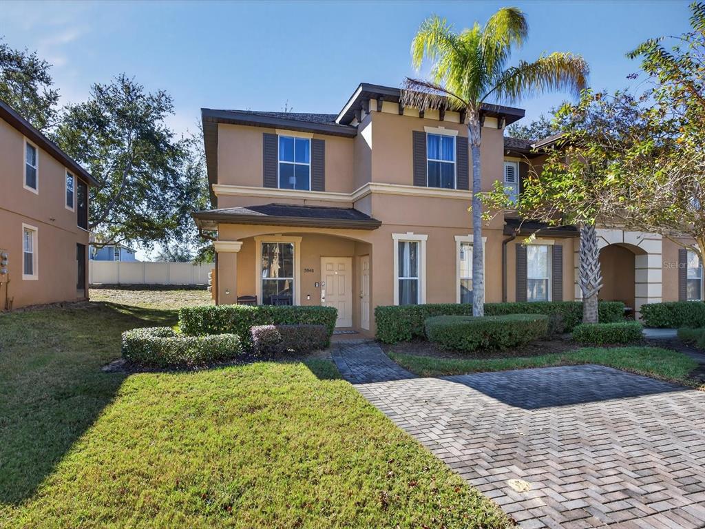 A two-story tan stucco townhouse features a brick paver driveway and a palm tree — 3948 CALABRIA AVENUE, DAVENPORT, FL