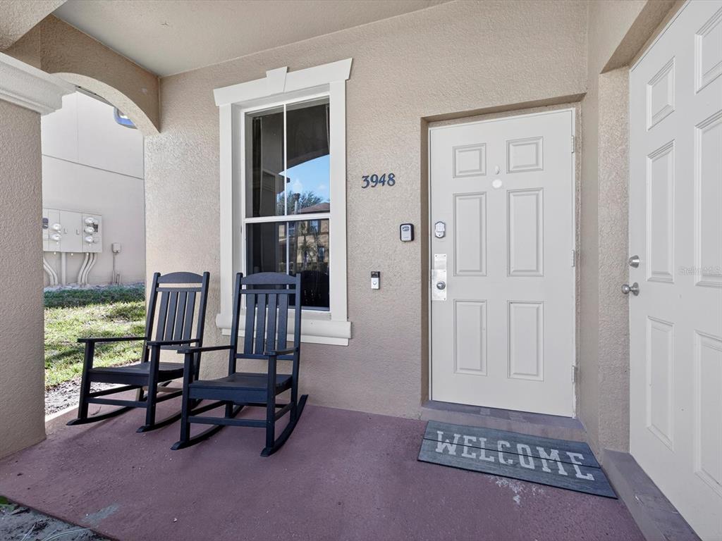 A covered front porch features two black rocking chairs, a window, and a white door — 3948 CALABRIA AVENUE, DAVENPORT, FL