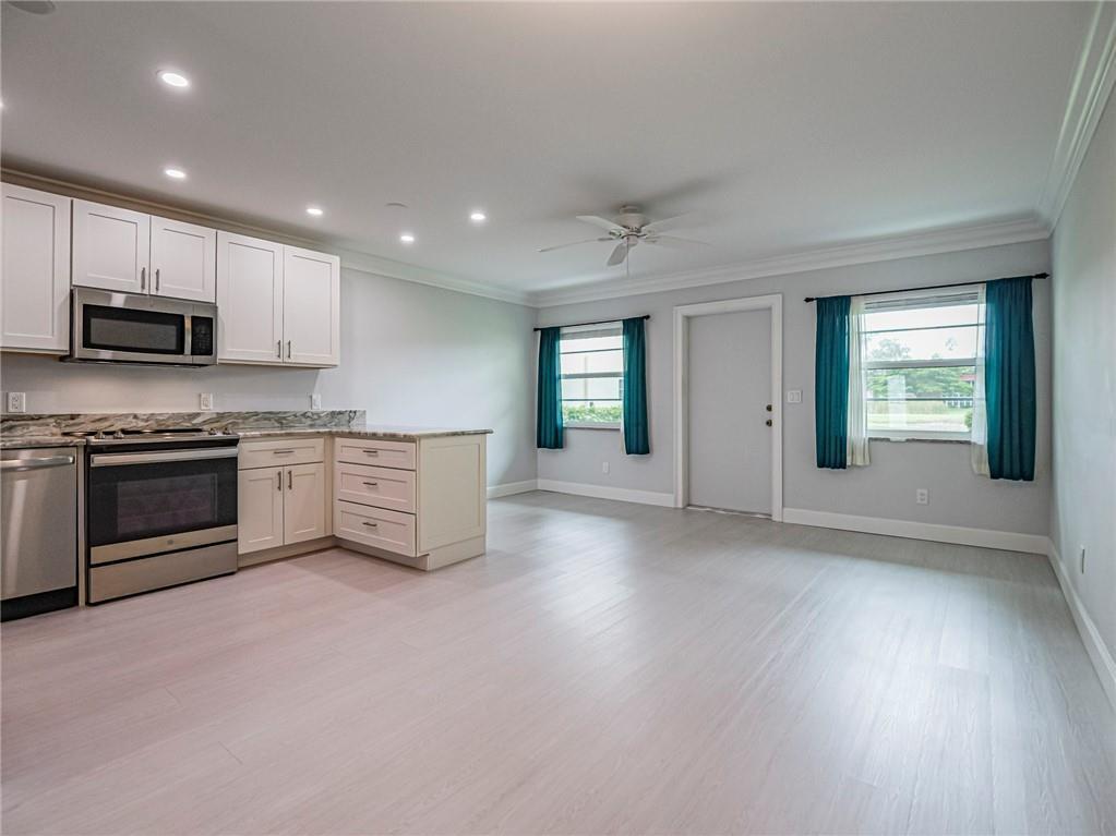 A kitchen with white cabinets and stainless steel appliances opens into a spacious living area — 97 Spring Lake Drive # 104, Vero Beach FL 32962, VERO BEACH, FL