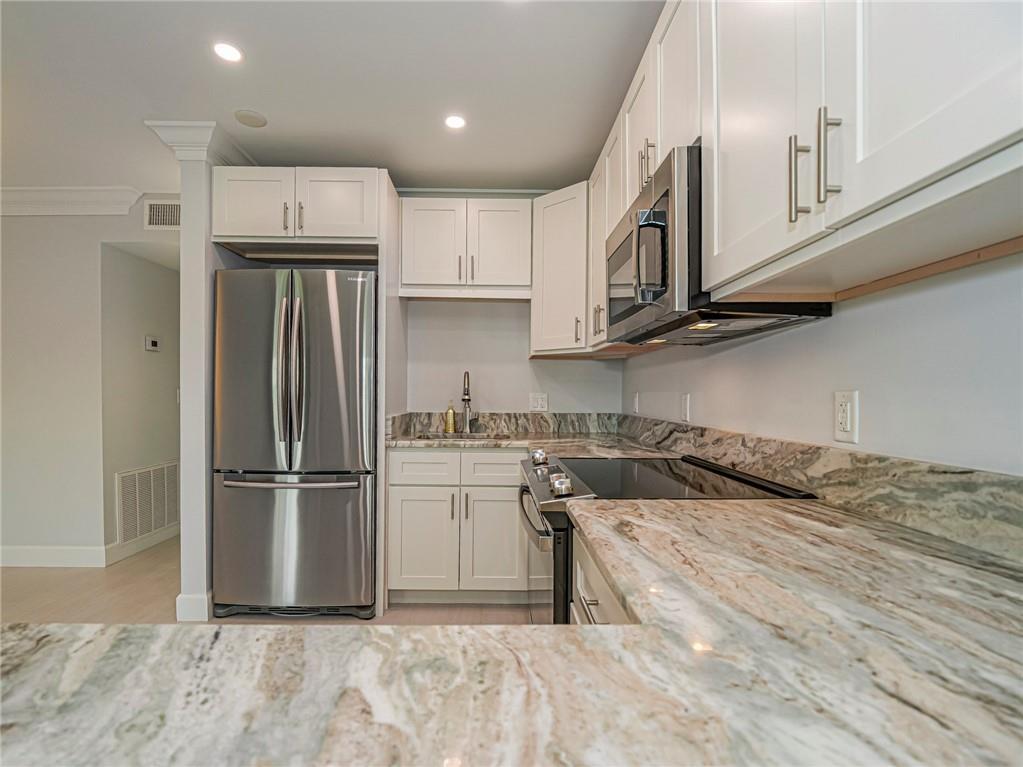 A kitchen features white cabinets, stainless steel appliances, and patterned stone countertops — 97 Spring Lake Drive # 104, Vero Beach FL 32962, VERO BEACH, FL