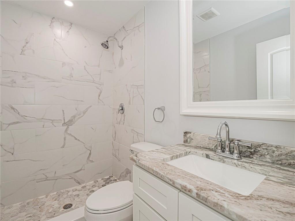 A bathroom features a marble-tiled shower with a pebble floor, a vanity, and a mirror — 97 Spring Lake Drive # 104, Vero Beach FL 32962, VERO BEACH, FL