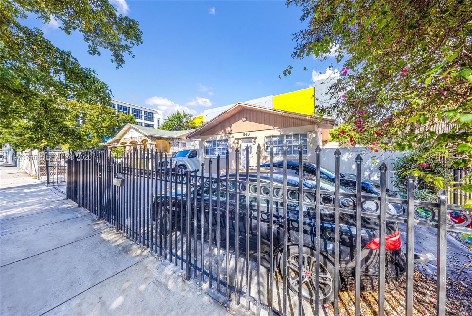 A single-story house with a tan facade and a black metal fence in the foreground — 1143 NW 6th St, Miami FL 33136, MIAMI, FL