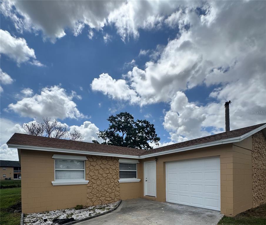 A single-story house with tan block walls, stone accents, a white garage door, and roof — 5693 TULIP AVENUE, ORLANDO, FL