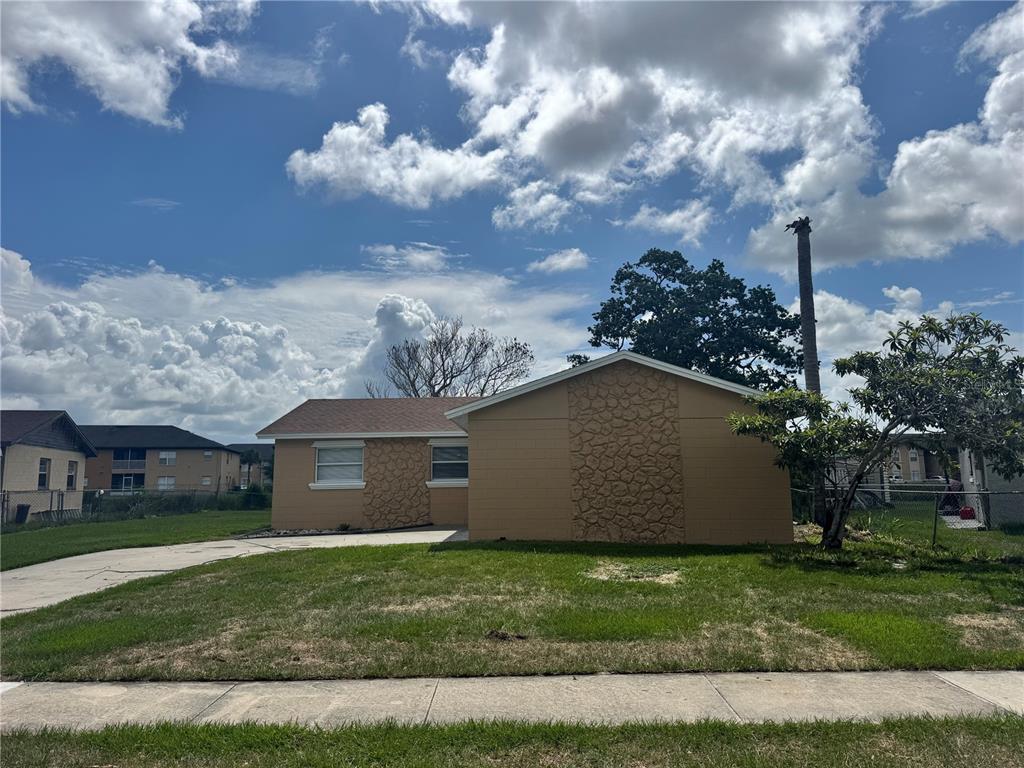 A single-story house with tan walls, stone accents, and a driveway under a cloudy sky — 5693 TULIP AVENUE, ORLANDO, FL