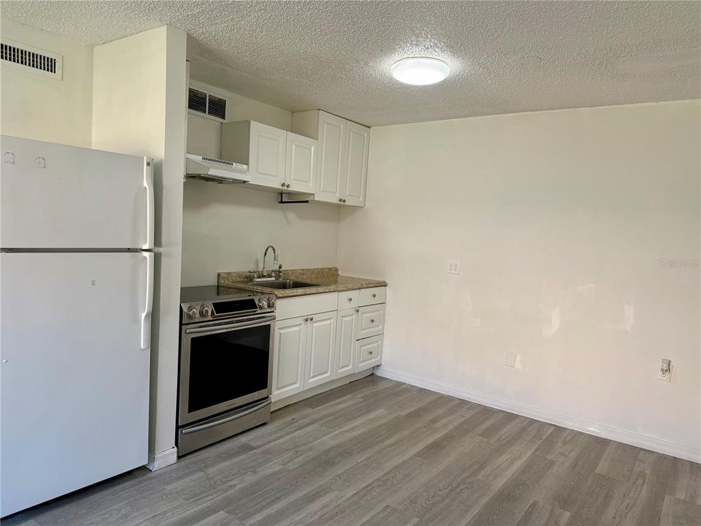 A small kitchen features white cabinets, stainless steel appliances, and light-colored wood-look flooring — 9013 WESTCHESTER CIRCLE UNIT 32, TAMPA, FL