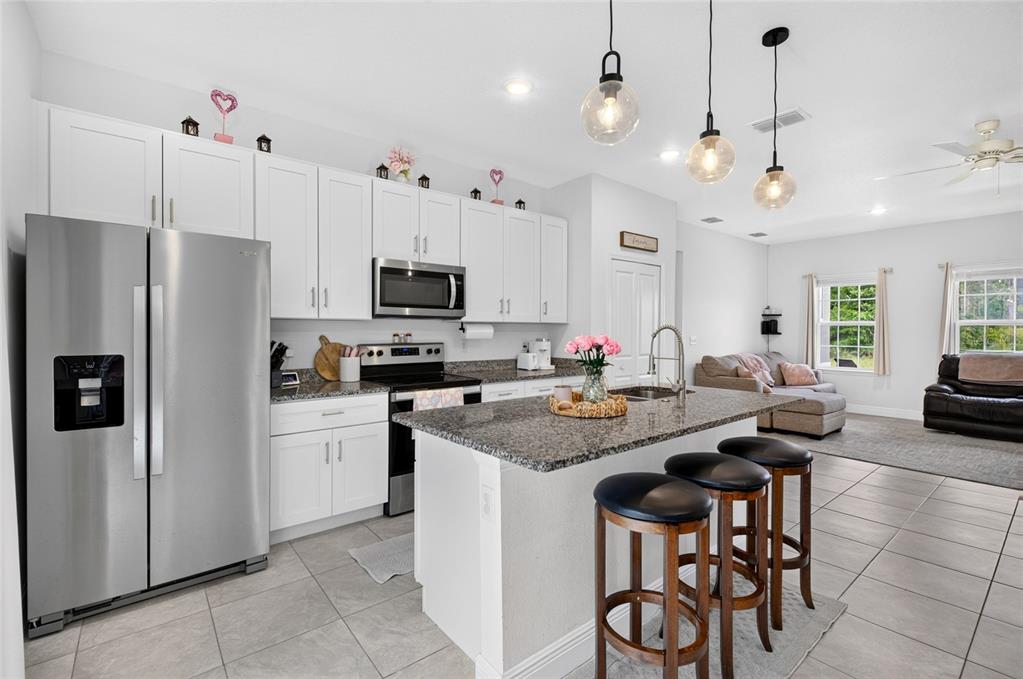 A kitchen with white cabinets, granite countertops, and an island with three bar stools — 13669 SW 81ST CIRCLE, OCALA, FL