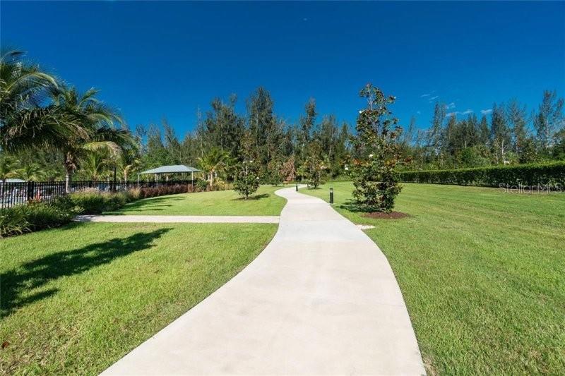 A concrete path winds through a grassy lawn toward trees and a shaded pavilion — 7104 W LENOX CIRCLE, PUNTA GORDA, FL
