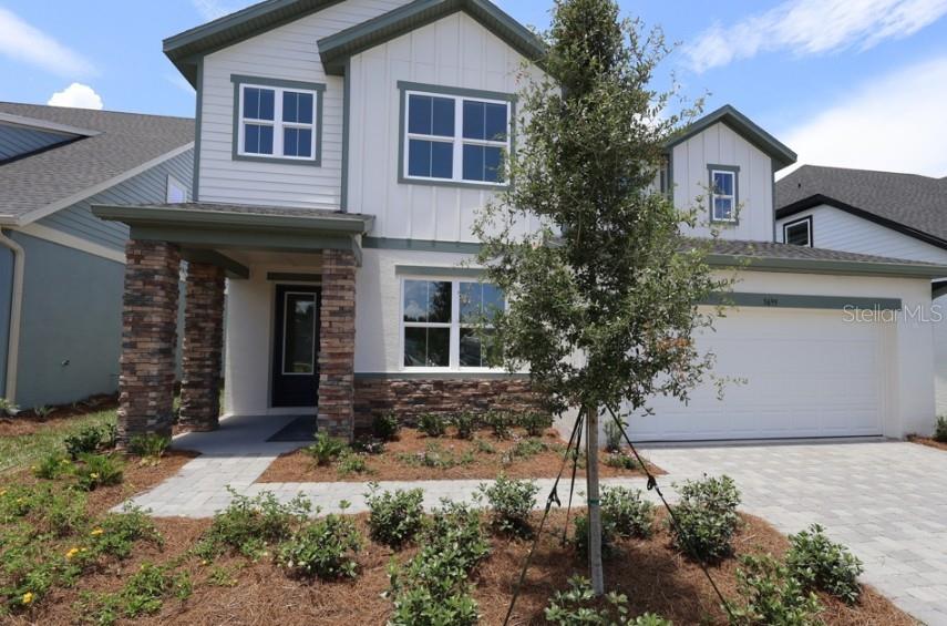 A two-story house features white vertical siding, stone accents, a front porch, and a garage — 5699 LEAFLET TRAIL, MOUNT DORA, FL