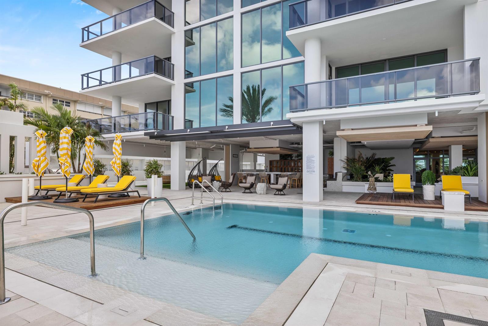 A modern apartment building features a swimming pool with lounge chairs and a covered patio — 305 Briny Avenue # 506, Pompano Beach FL 33062, POMPANO BEACH, FL