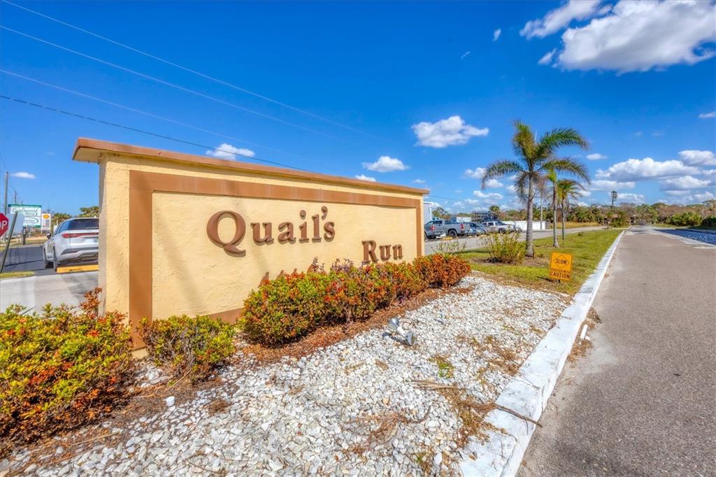 A beige monument sign for Quail's Run stands beside a road under a blue sky — 12 QUAILS RUN BOULEVARD UNIT 7, ENGLEWOOD, FL