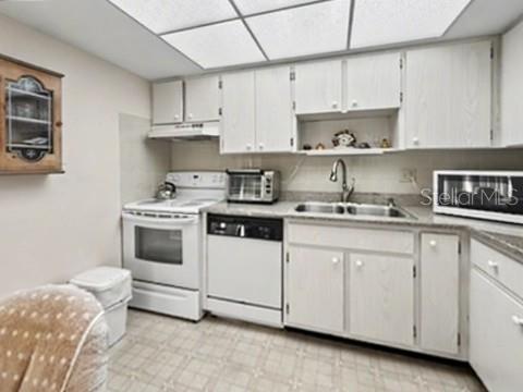 A kitchen features white cabinets, a white stove, a dishwasher, and a double sink — 12 QUAILS RUN BOULEVARD UNIT 7, ENGLEWOOD, FL