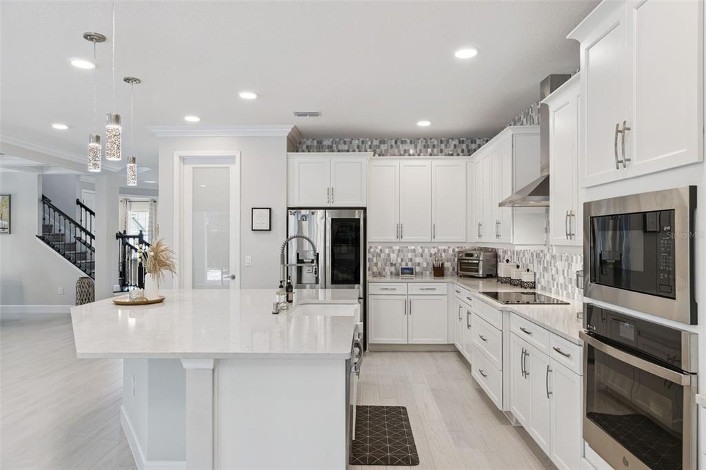 A modern white kitchen features a large island, quartz countertops, and stainless steel appliances — 3336 LONE CYPRESS POINT, OVIEDO, FL