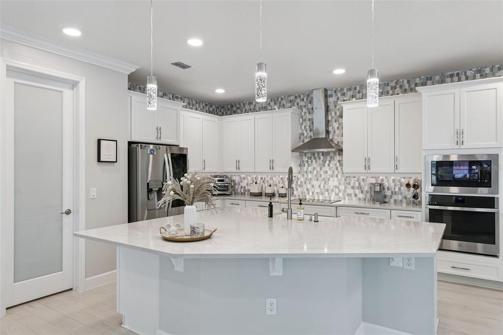 A modern kitchen features white cabinetry, a large quartz island, and a mosaic tile backsplash — 3336 LONE CYPRESS POINT, OVIEDO, FL