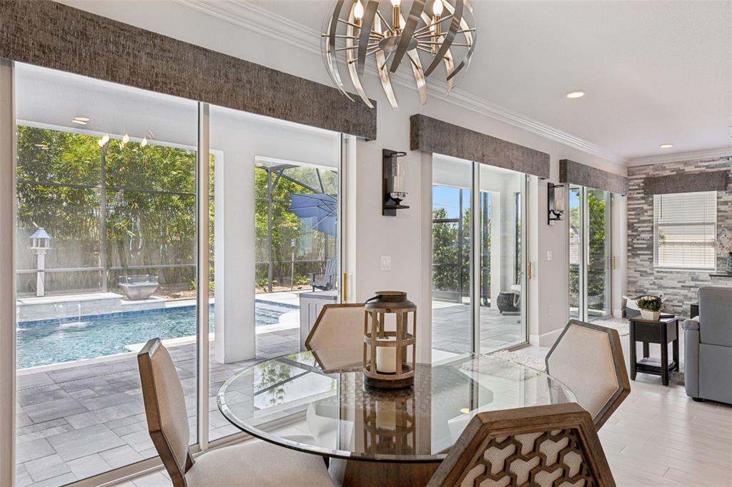 A dining area with a glass table, modern chandelier, and sliding doors overlooking a pool — 3336 LONE CYPRESS POINT, OVIEDO, FL