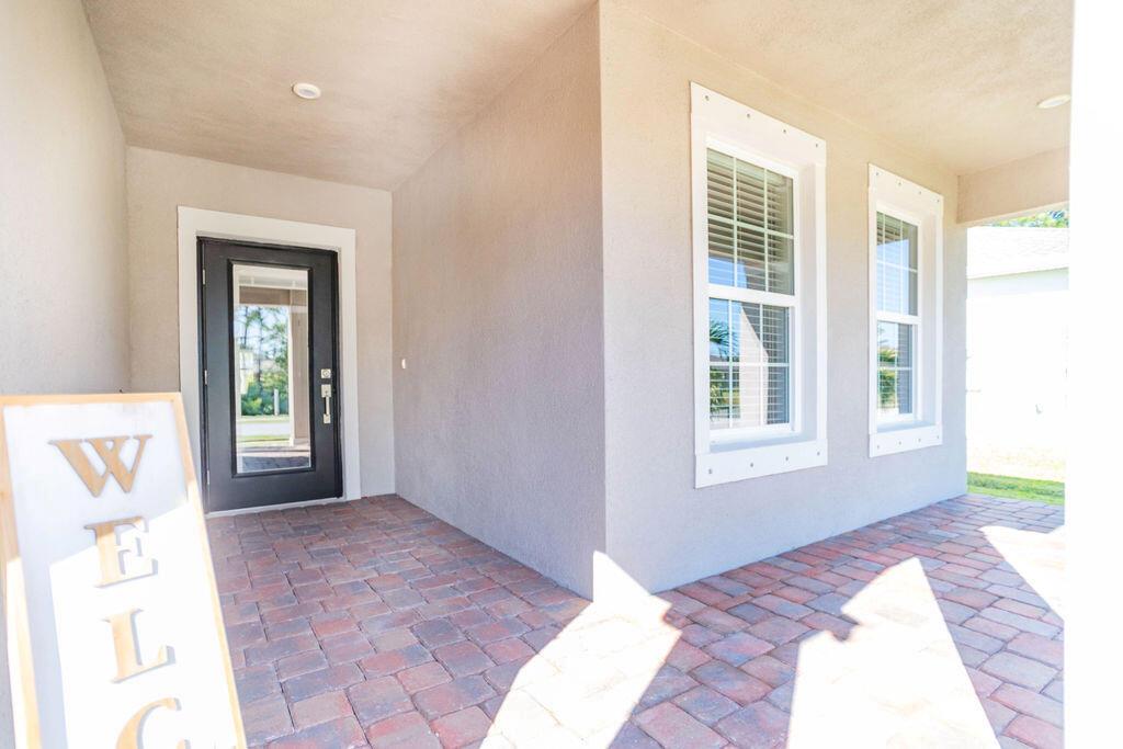 A covered front porch features a brick paver floor, a black door, and two windows — 4198 Keeson Circle, Vero Beach FL 32967, VERO BEACH, FL
