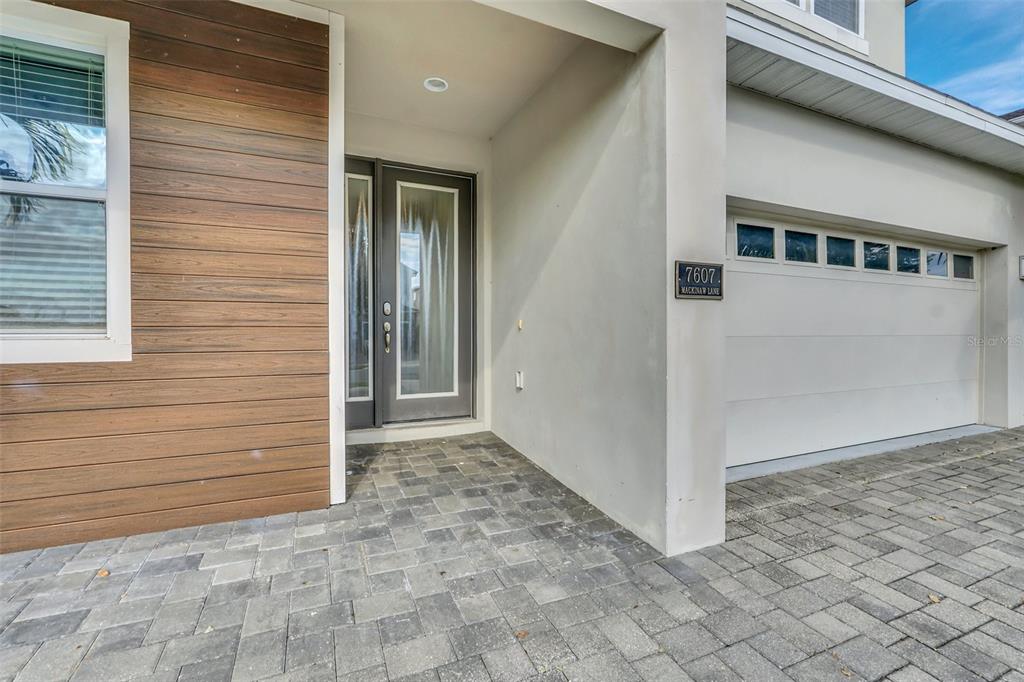 A modern home exterior features a paved driveway, a garage, and a wood-paneled entryway — 7607 MACKINAW LANE, KISSIMMEE, FL