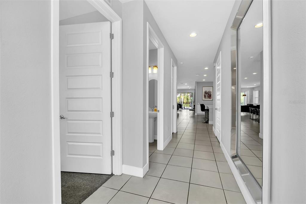 A hallway with light tile flooring, white walls, and a large wall-mounted mirror — 7607 MACKINAW LANE, KISSIMMEE, FL