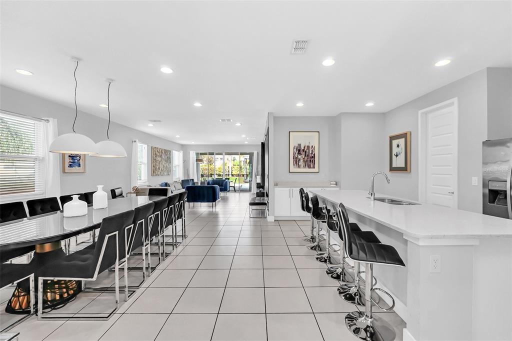 A modern open-concept kitchen and dining area with tile flooring, white cabinetry, and bar seating — 7607 MACKINAW LANE, KISSIMMEE, FL