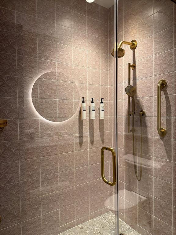 A shower with pink patterned tiles, brass fixtures, a grab bar, and a circular light — 3151 SUNSET WALK DR UNIT 516, KISSIMMEE, FL