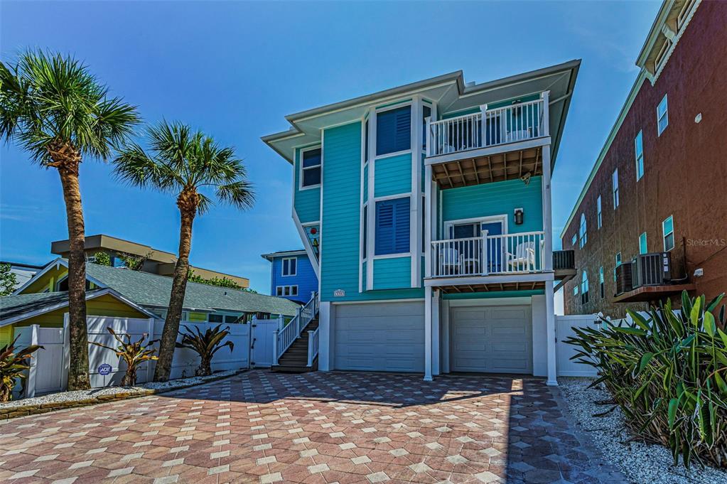A three-story turquoise house features a paved driveway, two garage doors, and two stacked balconies — 13303 GULF LANE, MADEIRA BEACH, FL