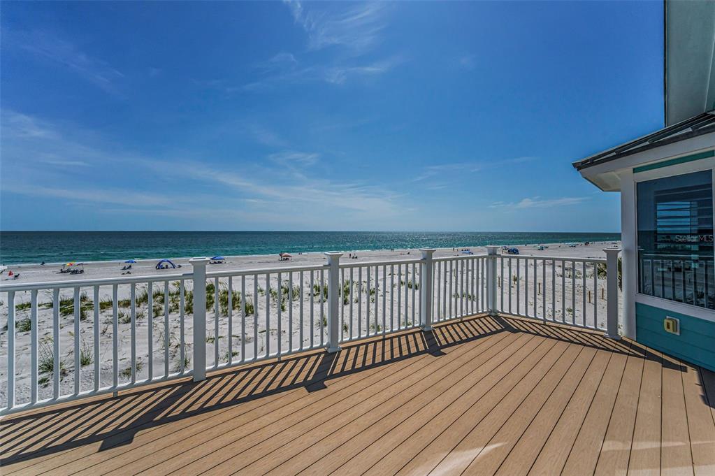 A wooden deck with a white railing overlooks a sandy beach and the ocean — 13303 GULF LANE, MADEIRA BEACH, FL