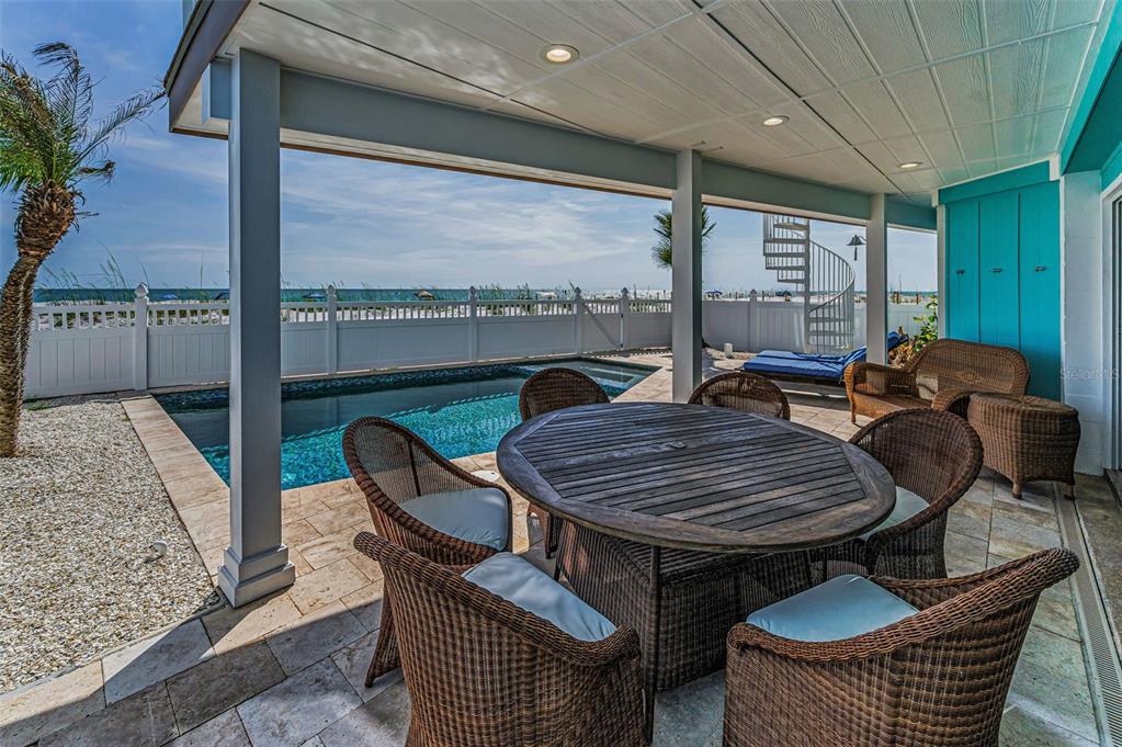 A covered patio features a dining set, wicker chairs, a swimming pool, and ocean views — 13303 GULF LANE, MADEIRA BEACH, FL