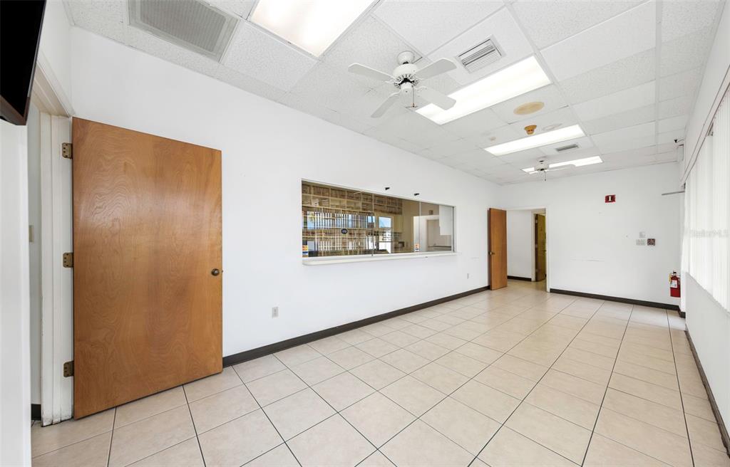 An empty office room features white walls, tiled floors, a ceiling fan, and a service window — 655 N INDIANA AVENUE, ENGLEWOOD, FL