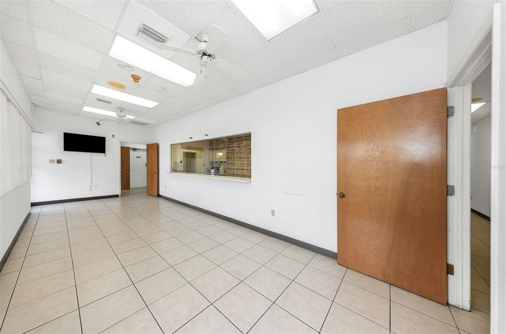 An empty office space features white walls, tiled flooring, a service window, and ceiling fans — 655 N INDIANA AVENUE, ENGLEWOOD, FL