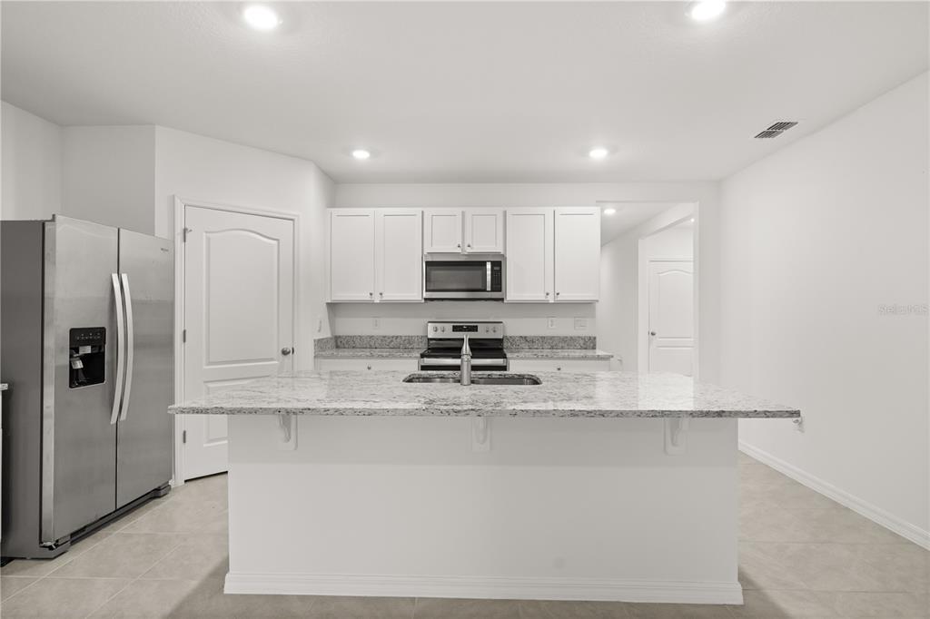 A kitchen features white cabinets, granite countertops, a center island, and stainless steel appliances — 1340 BLADON AVENUE, DELTONA, FL