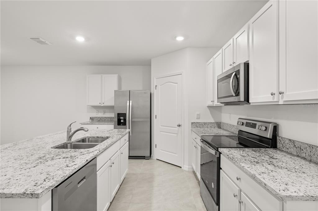 A kitchen featuring white cabinets, granite countertops, stainless steel appliances, and a central island — 1340 BLADON AVENUE, DELTONA, FL