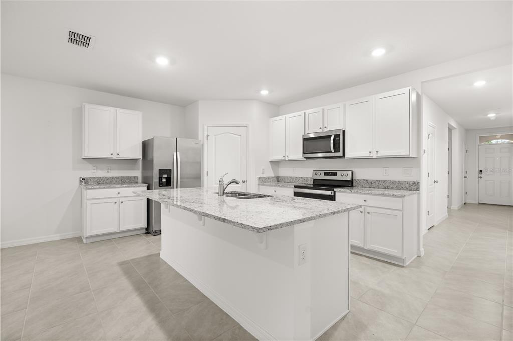 A kitchen with white cabinets, granite countertops, a central island, and stainless steel appliances — 1340 BLADON AVENUE, DELTONA, FL