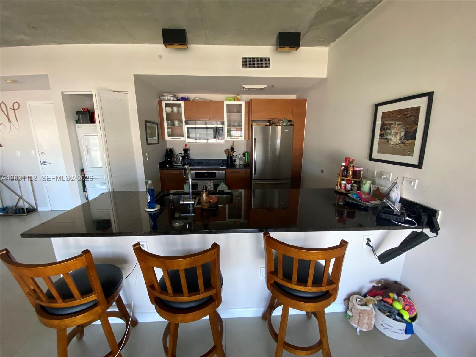 A kitchen features dark wood cabinets, black countertops, stainless steel appliances, and three wooden barstools — 3451 NE 1st Ave # M0906, Miami FL 33137, MIAMI, FL