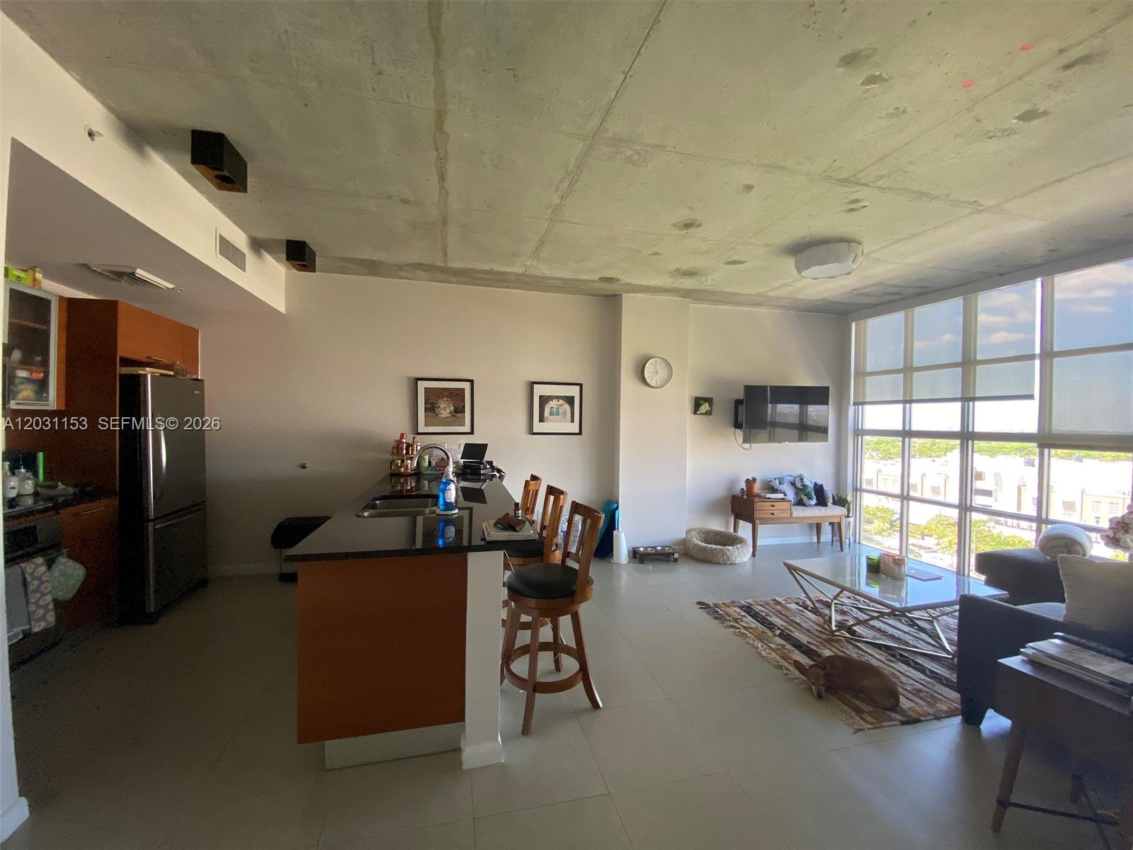 This open-concept living area features a kitchen island, concrete ceilings, and floor-to-ceiling windows — 3451 NE 1st Ave # M0906, Miami FL 33137, MIAMI, FL