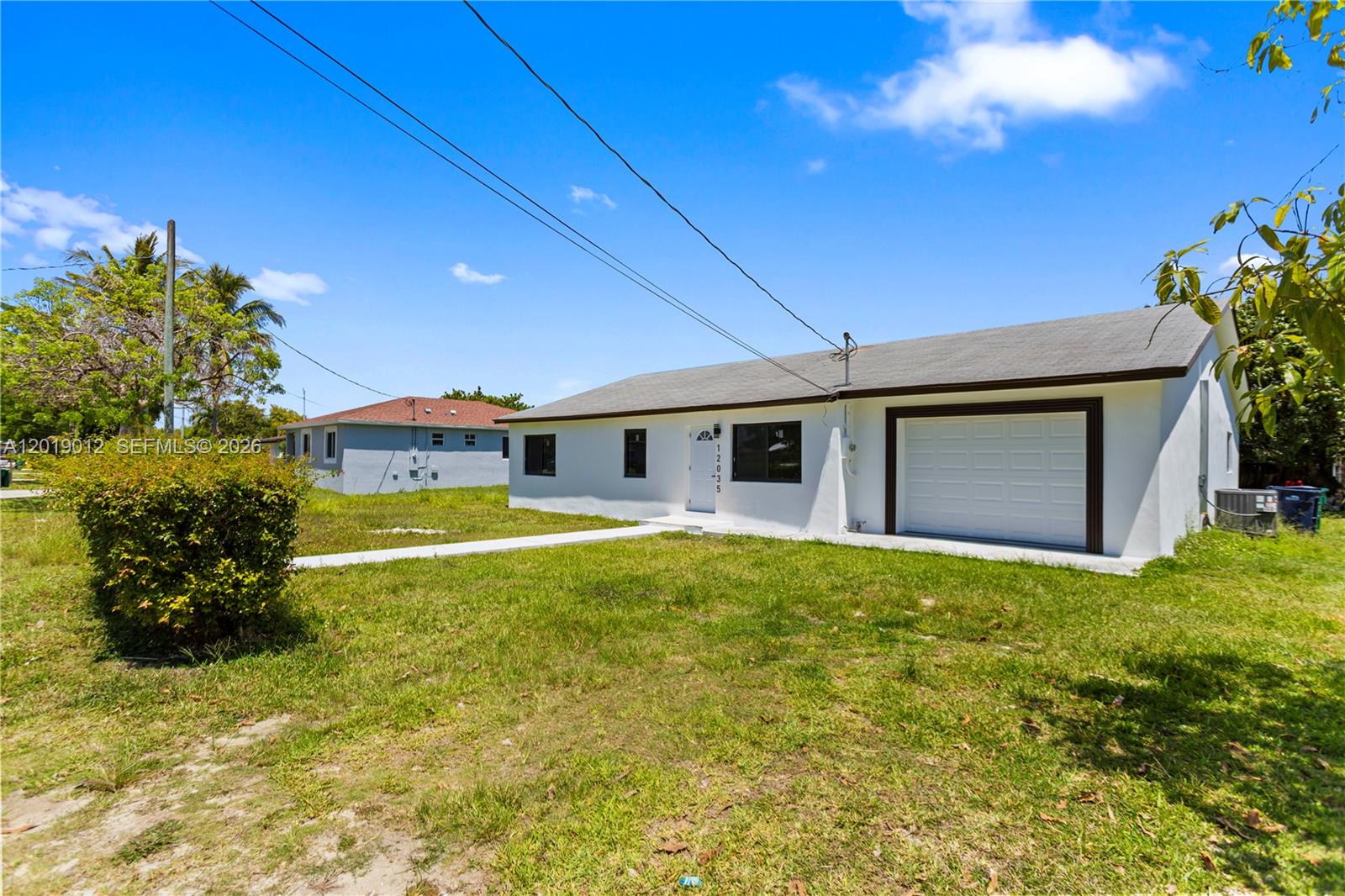 A white single-story house features a front-facing garage and a concrete walkway on a lawn — 12035 SW 214th Ter, Miami FL 33177, MIAMI, FL