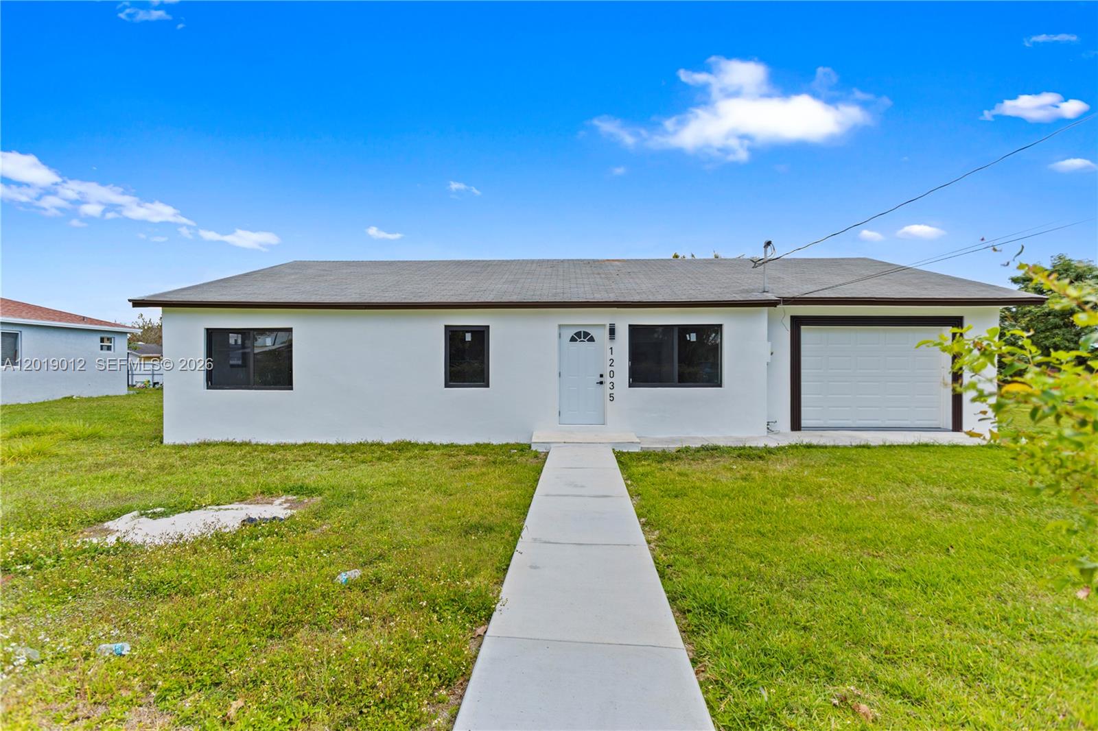 A single-story white house features a front door, a garage, and a concrete walkway — 12035 SW 214th Ter, Miami FL 33177, MIAMI, FL