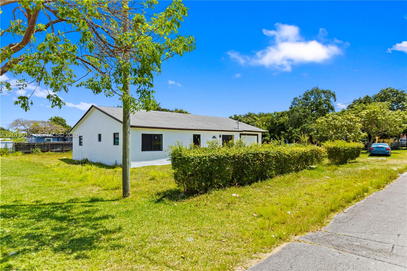 A white single-story house with a gray roof sits behind a hedge on a lawn — 12035 SW 214th Ter, Miami FL 33177, MIAMI, FL
