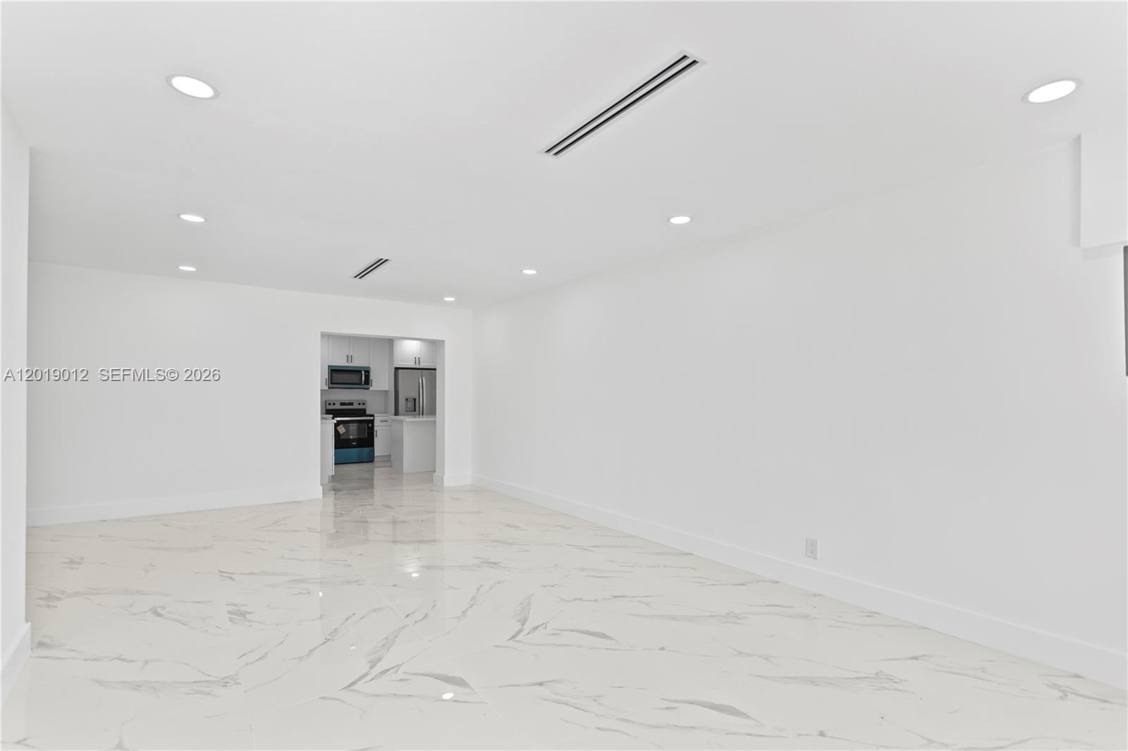 A bright, empty room features white walls, recessed lighting, and white marble-patterned tile flooring — 12035 SW 214th Ter, Miami FL 33177, MIAMI, FL