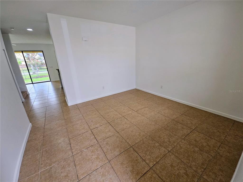 An empty room with tan tile flooring and white walls leads to a sliding glass door — 1899 PORTOFINO MEADOWS BOULEVARD, ORLANDO, FL