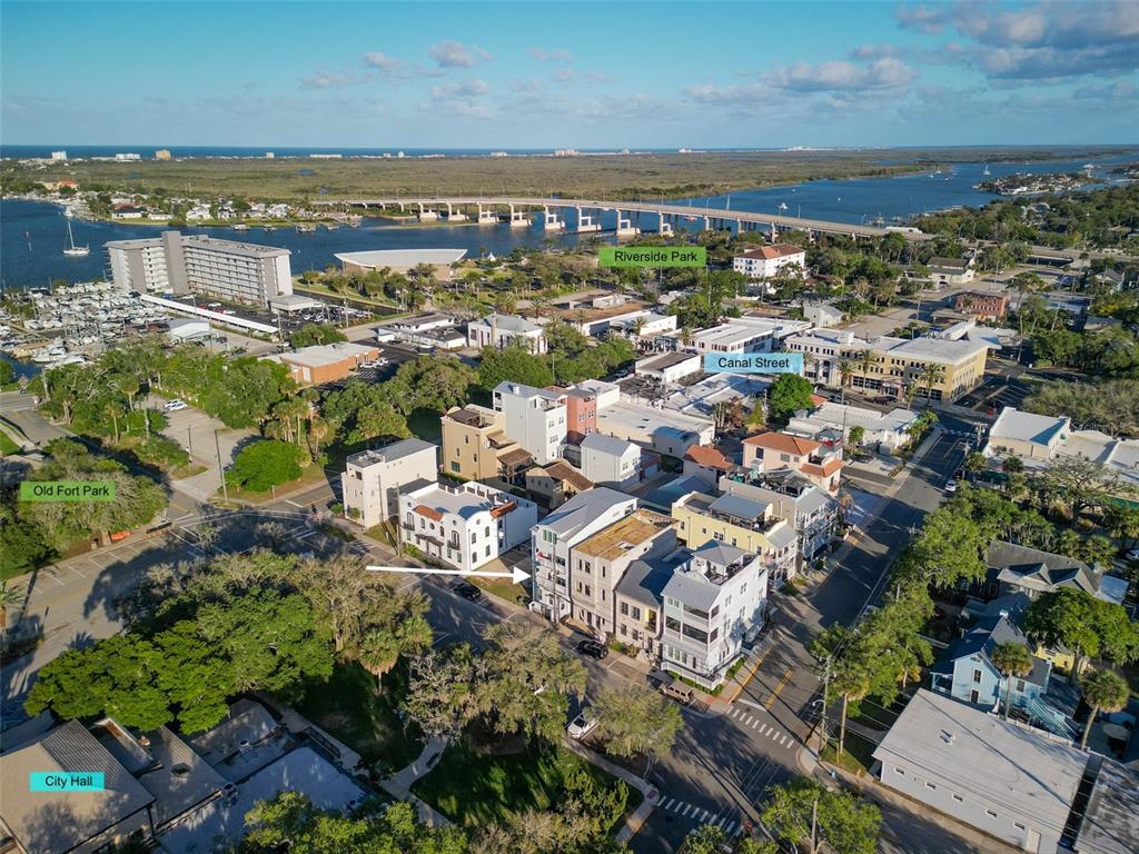 An aerial view shows multi-story buildings near a park, city hall, and a waterfront bridge — 140 JULIA STREET, NEW SMYRNA BEACH, FL