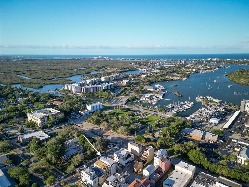 An aerial view shows a coastal town with a marina, wetlands, and residential buildings — 140 JULIA STREET, NEW SMYRNA BEACH, FL