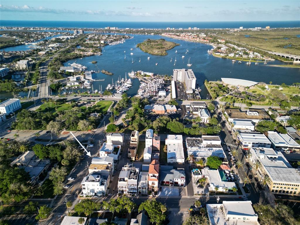 An aerial view shows a coastal town with a marina, buildings, and a white arrow — 140 JULIA STREET, NEW SMYRNA BEACH, FL