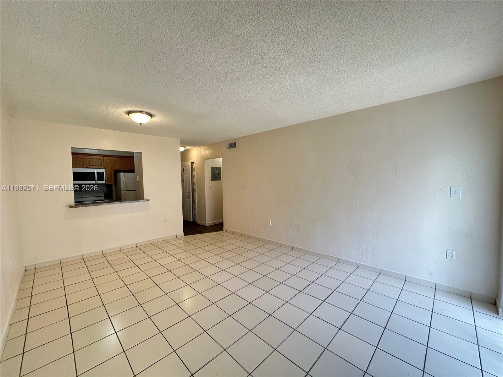 An empty living area features white tiled floors, a popcorn ceiling, and a kitchen pass-through — 1008 NW 45th Ave # 08, Miami FL 33126, MIAMI, FL