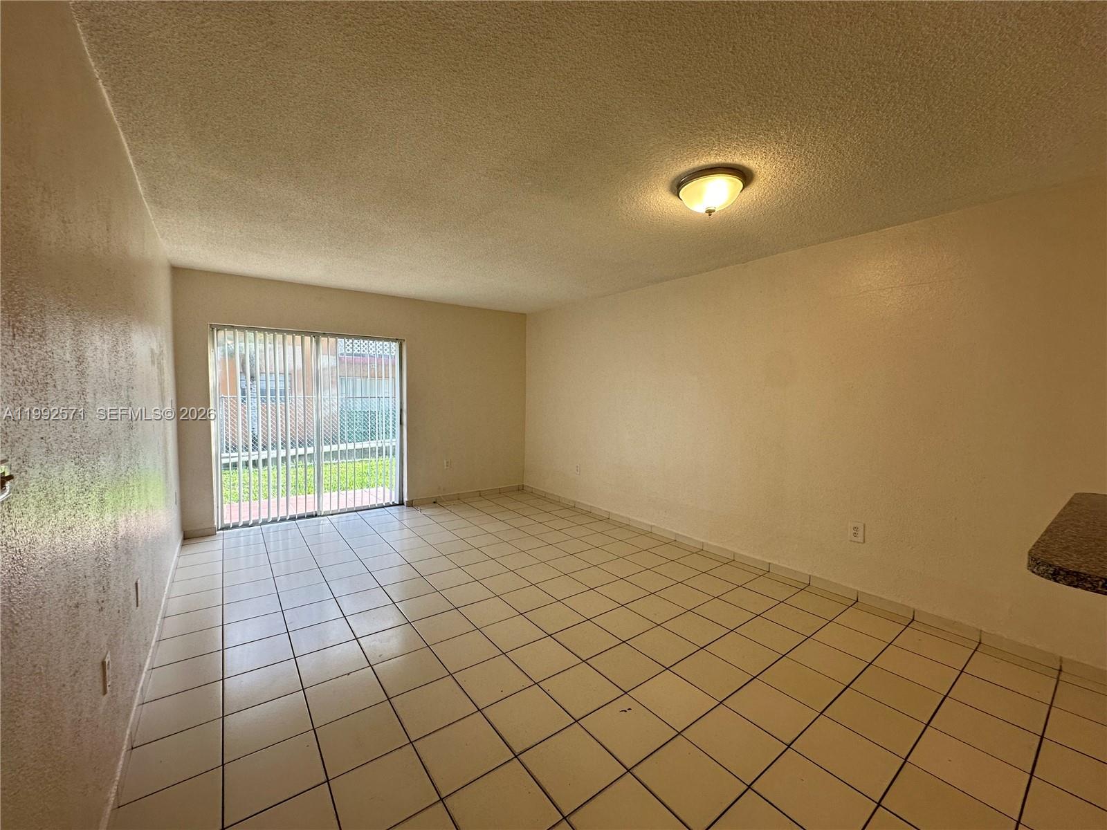 An empty room features white tiled floors, beige walls, and a sliding glass door — 1008 NW 45th Ave # 08, Miami FL 33126, MIAMI, FL