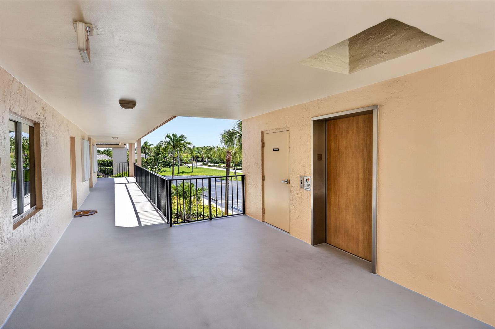 An outdoor apartment building walkway features a wooden elevator door and a metal railing — 275 Palm Avenue # D, Jupiter FL 33477, JUPITER, FL