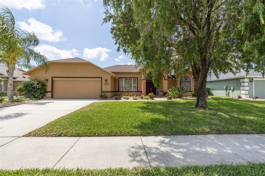 A single-story tan house with a two-car garage and a large tree in the yard — 1887 CREEKWATER BOULEVARD, PORT ORANGE, FL